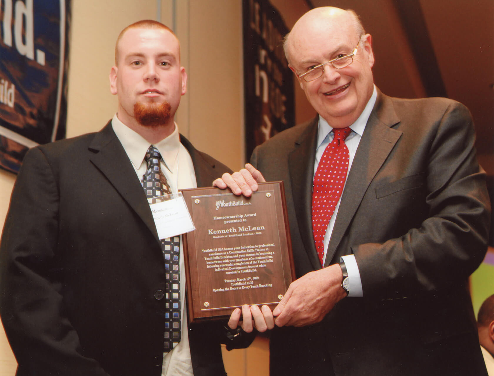 Two men in suits pose with an award plaque.