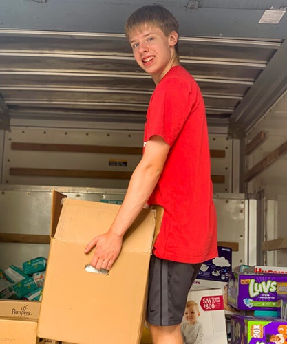 A young man in a red T-shirt loads boxes of diapers into a truck.