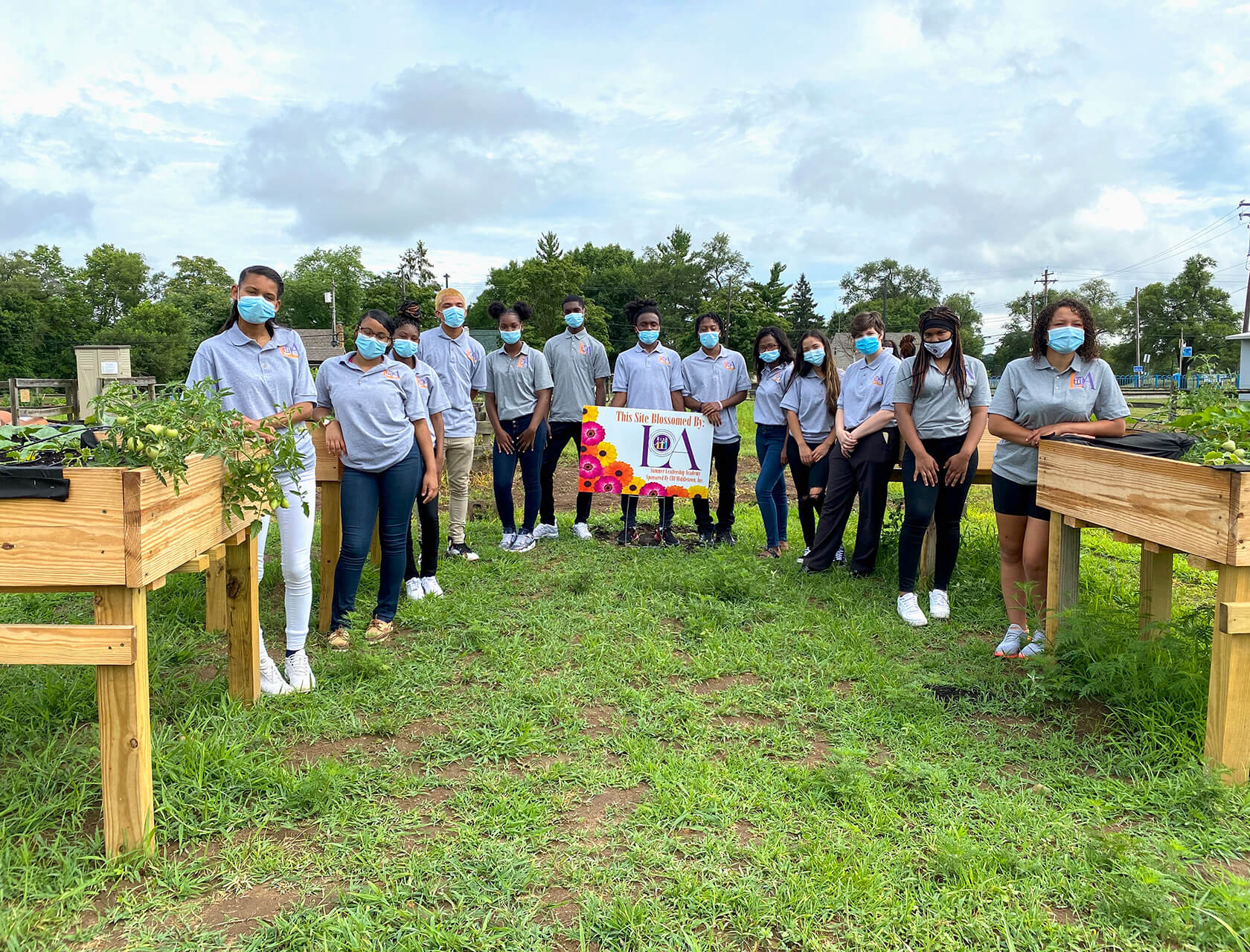 Students in matching grey polo shirts stand among raised garden beds.