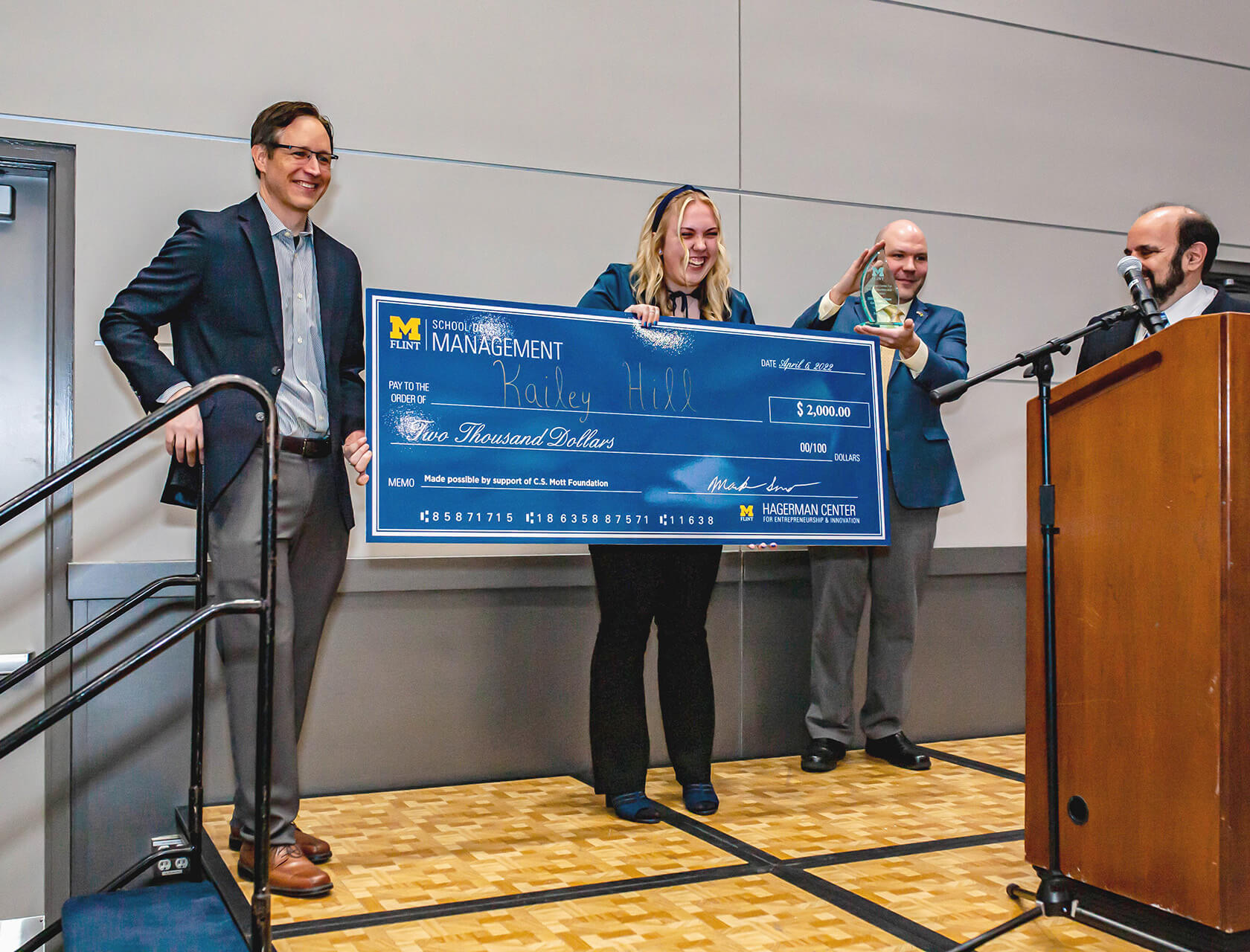 A young woman holds a giant blue check for $2,000.