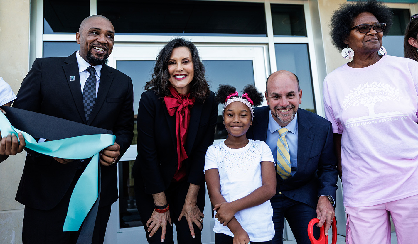Two men, two women and one student smile and bend down to the camera after having cut the ribbon at the opening ceremony for a school building.