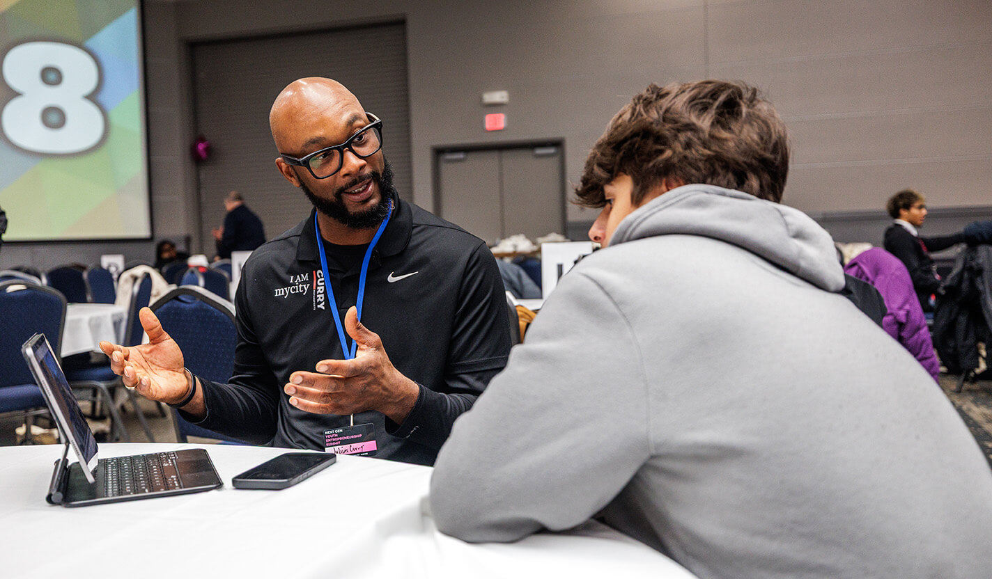Man in black collared shirt speaks to a student in a grey hoodie.