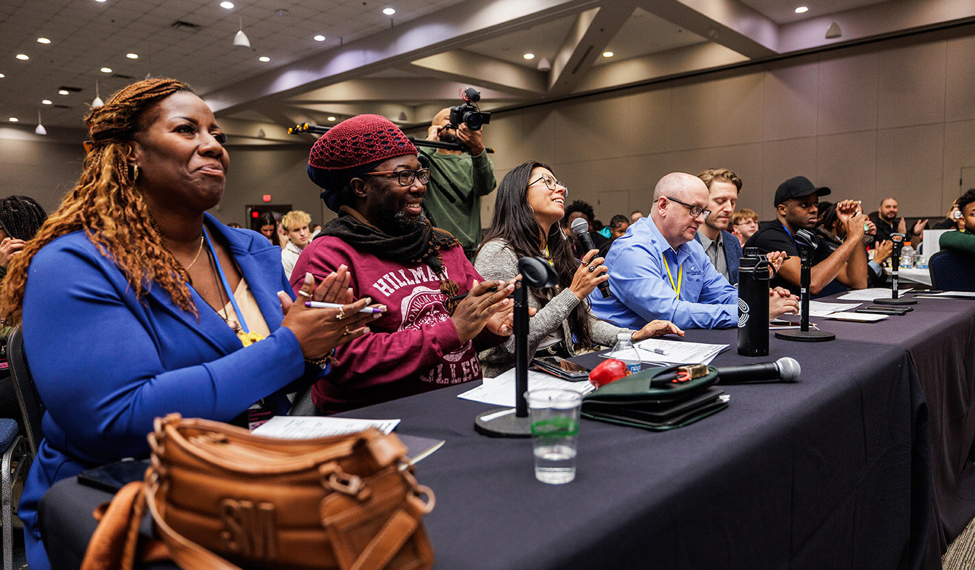 Six people sit at a long table, applauding.
