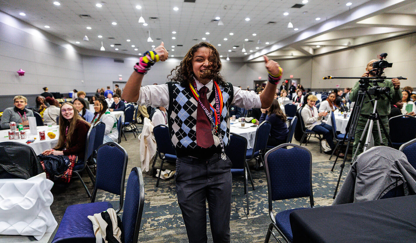 Young woman jumps with excitement, showing two thumbs up.