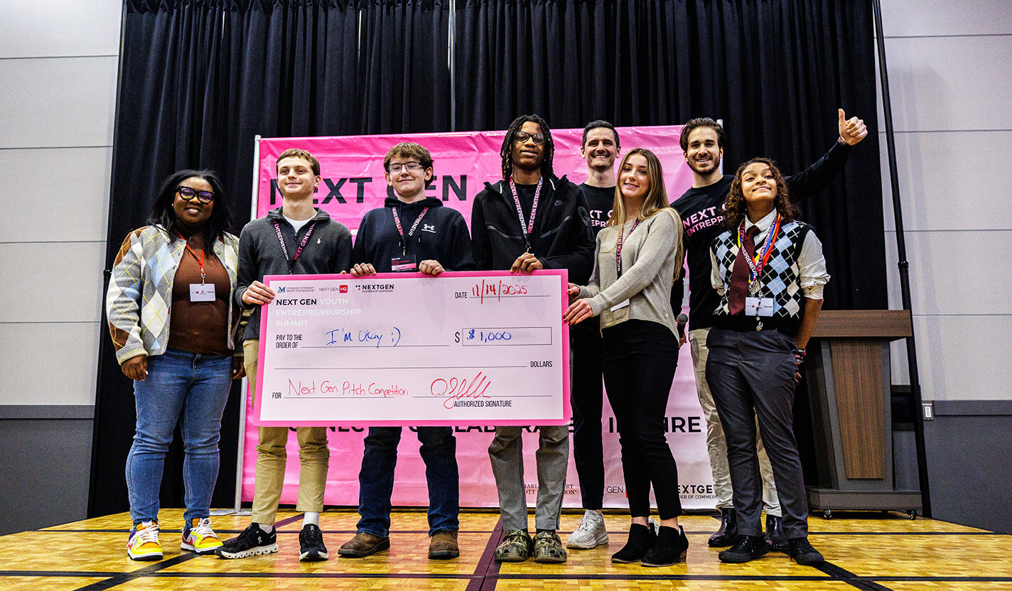 Students on stage hold up a giant pink check for $1,000