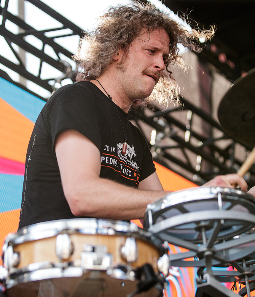 A man with long curly hair plays drums on stage at the Flint Alley Fest.