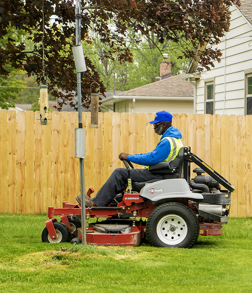 A man sits on a riding lawn mower and mowes a FLint resident's lawn.