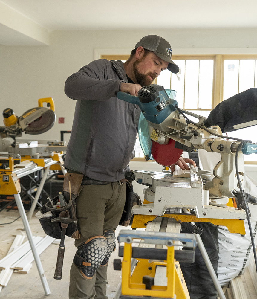 A man with a beard and work clothes uses a circular saw to cut trim for a home that is being remodeled in Flint's Carriage Town.