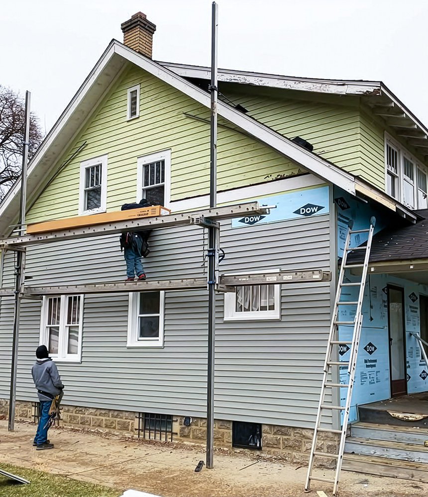 Flint home improvement workers add grey siding to an old two story home in Flint, MI.