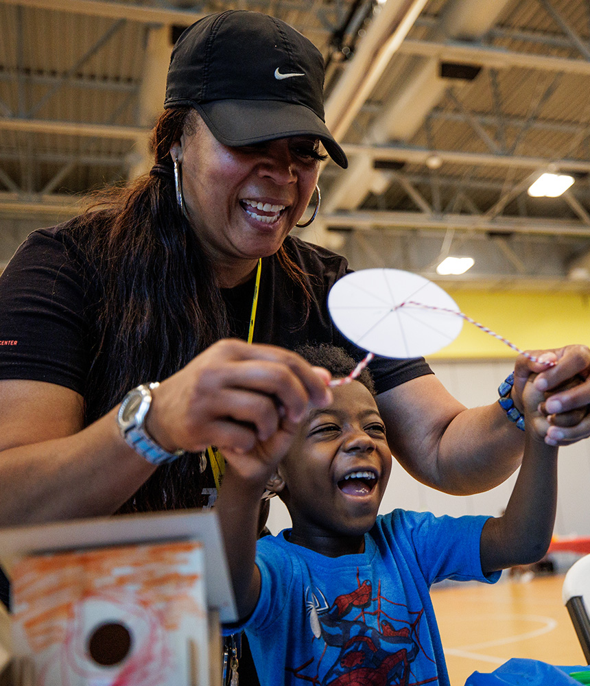 A teacher work with a young boy to twirl a paper wheel around a piece or red and white string