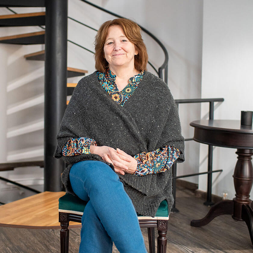 A woman sits in a chair in a modern room with a spiral staircase behind her.