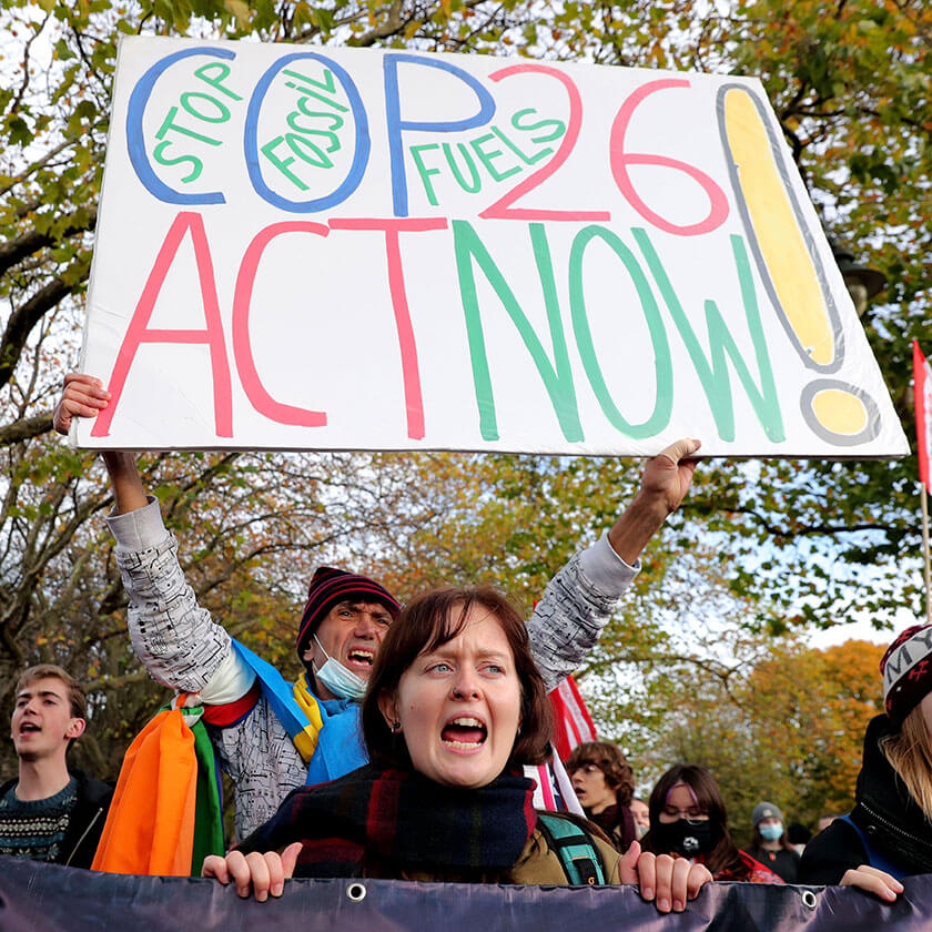 A group of protesters hold a sign reading "Stop fossil fuels, COP26 act now!" and a banner.