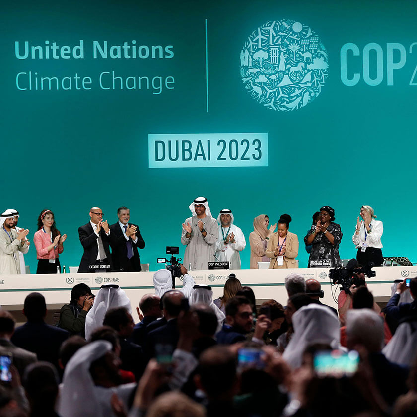 A group of people watch a row of people standing on a stage smile and applaud under signage that reads "United Nations Climate Change, Dubai 2023, COP28UAE."
