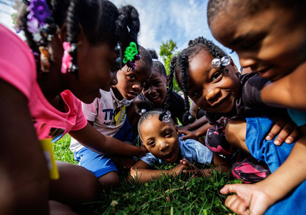 Seven kids smiling at the camera as they play on the grass.