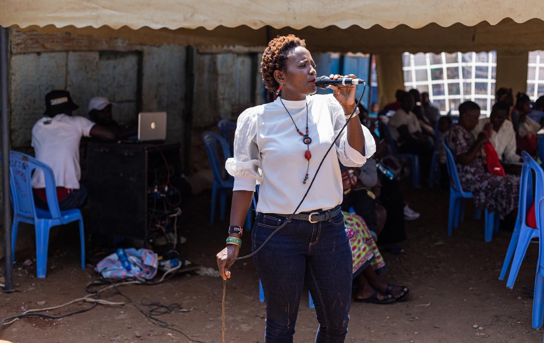 A woman speaks into an microphone, addressing people in community in the Dandora neighborhood of Nairobi, Kenya, about their rights.