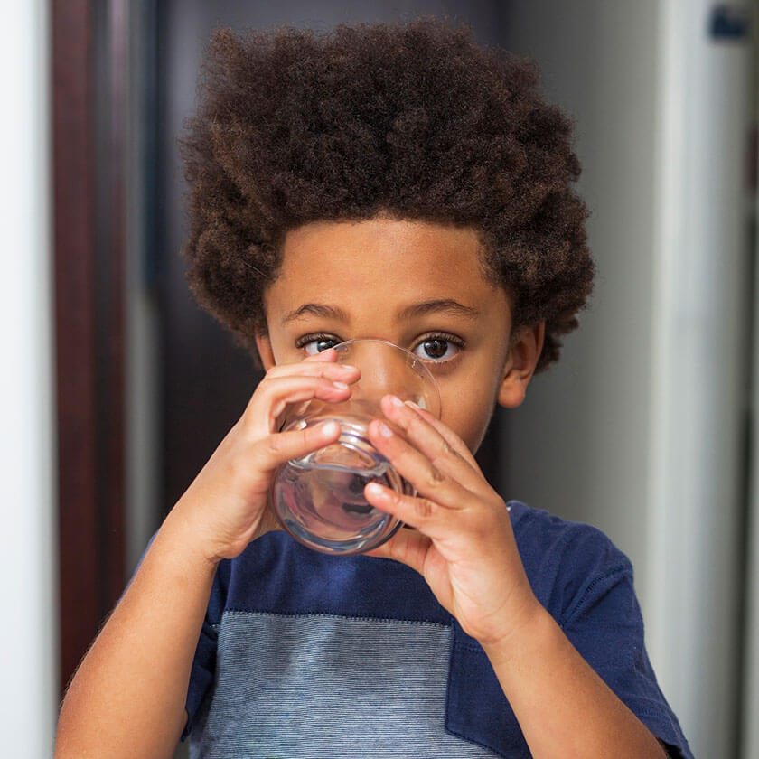 A young boy looks at the viewer over the glass of water he is drinking.