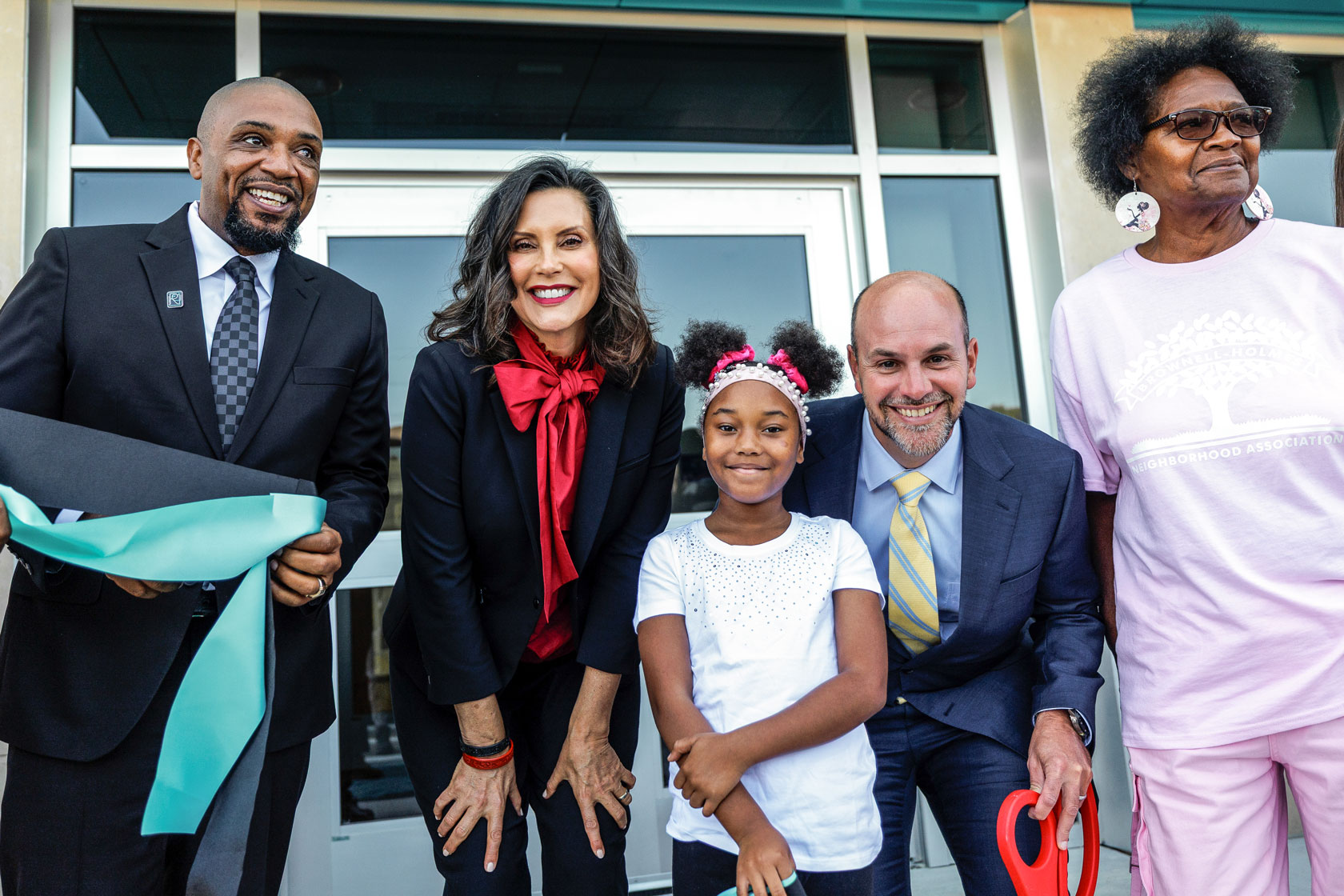 Two men, two women and one student smile and bend down to the camera after having cut the ribbon at the opening ceremony for a school building.
