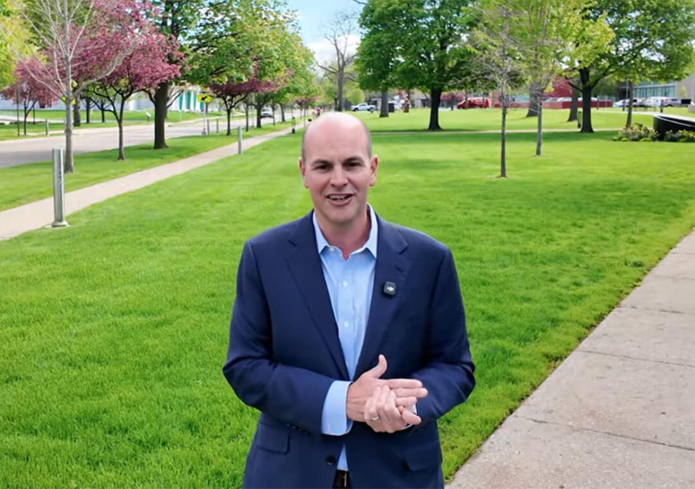 A man stands in a cultural center campus with greenery and flowering trees.
