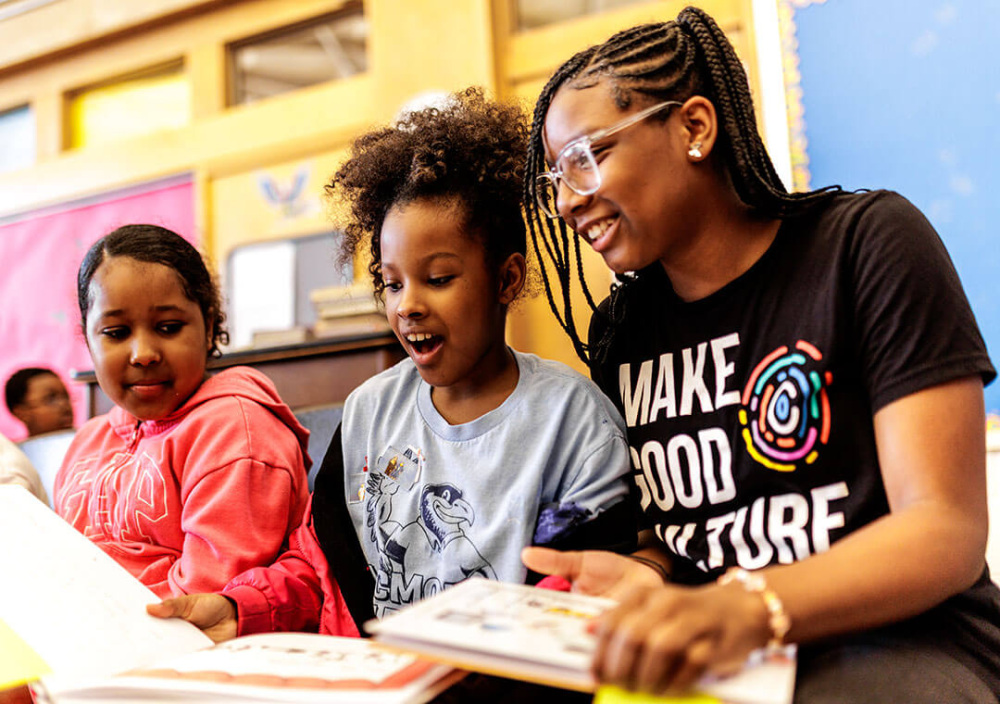 Three girls smile as they look through books.