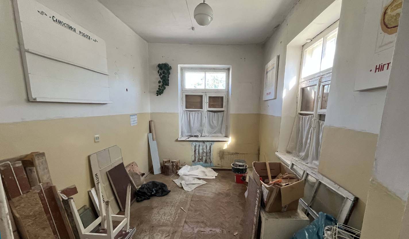 Interior room with worn floors, exposed materials, and stacked debris near windows, showing conditions before renovation in community foundation-supported housing for individuals receiving humanitarian relief assistance related to the war in Ukraine.