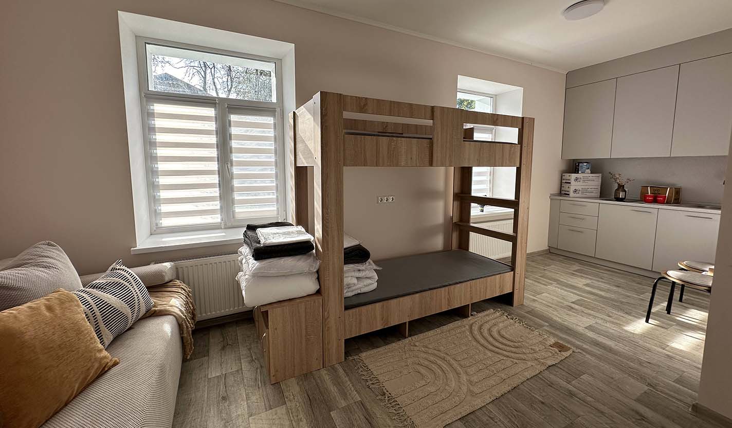 Bright, fully renovated interior room with a bunk bed, folded linens, and a kitchenette, showing completed community foundation-supported housing for individuals receiving humanitarian relief assistance related to the war in Ukraine.