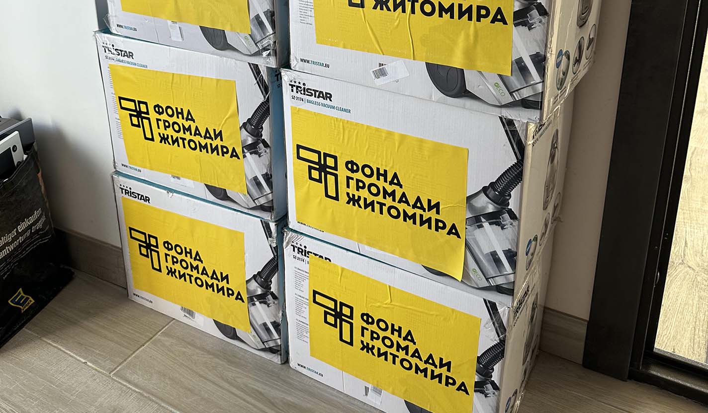 Stacked boxes labeled with a community organization sit inside a room, representing household supplies provided through community foundation-supported humanitarian relief for individuals affected by the war in Ukraine.
