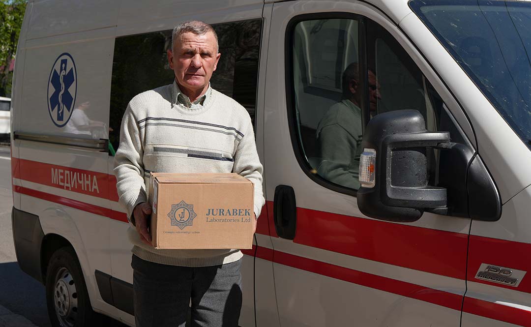 Person holds a box of medical supplies beside an ambulance van marked with emergency symbols, representing community foundation-supported humanitarian relief assistance related to the war in Ukraine.