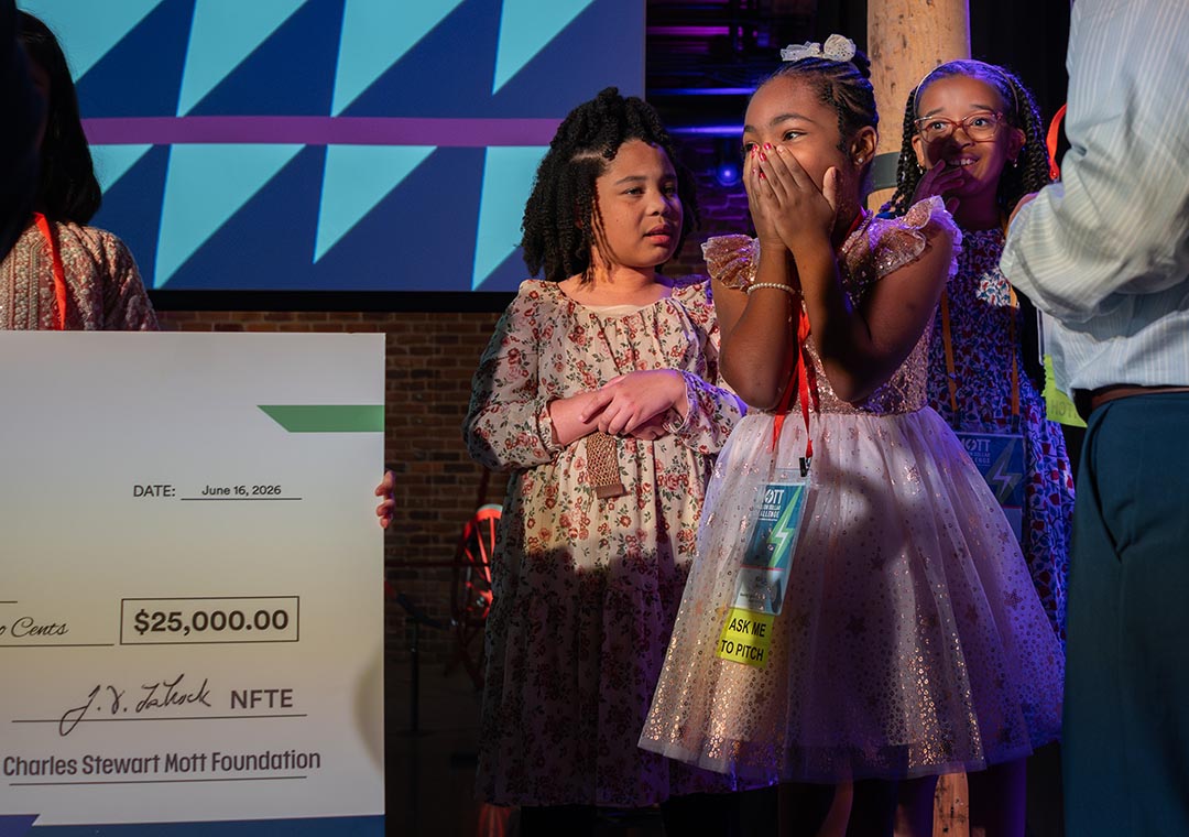 Young participants react excitedly on stage beside a large ceremonial check during an award presentation.