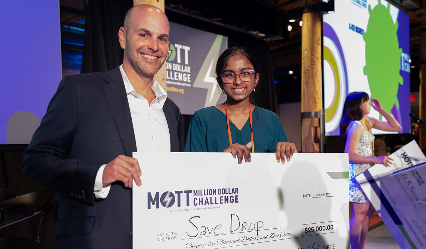 A student poses with an adult while holding a $25,000 award check for Save Drop.