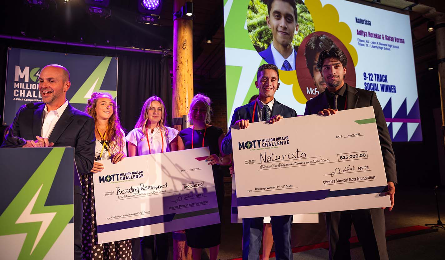 Student entrepreneurs hold large award checks on stage during the Mott Million Dollar Challenge awards ceremony.