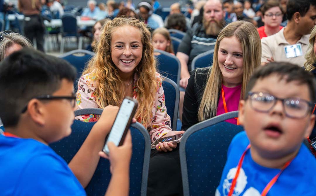 Two teens smile while talking with younger participants seated in front of them.