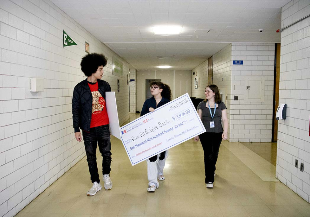 Youth Choice Awards recipients carry a ceremonial Charles Stewart Mott Foundation check for Glow Up & Give Back while walking through a school hallway.